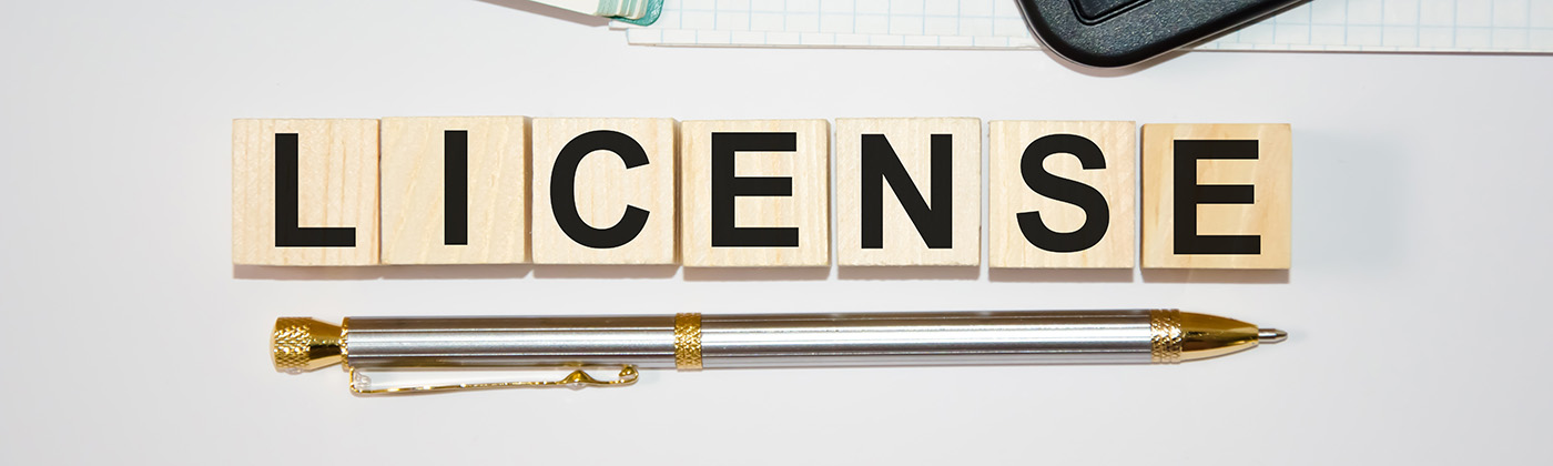 Wooden tiles spelling out the word license lay on a desktop with other business tools.